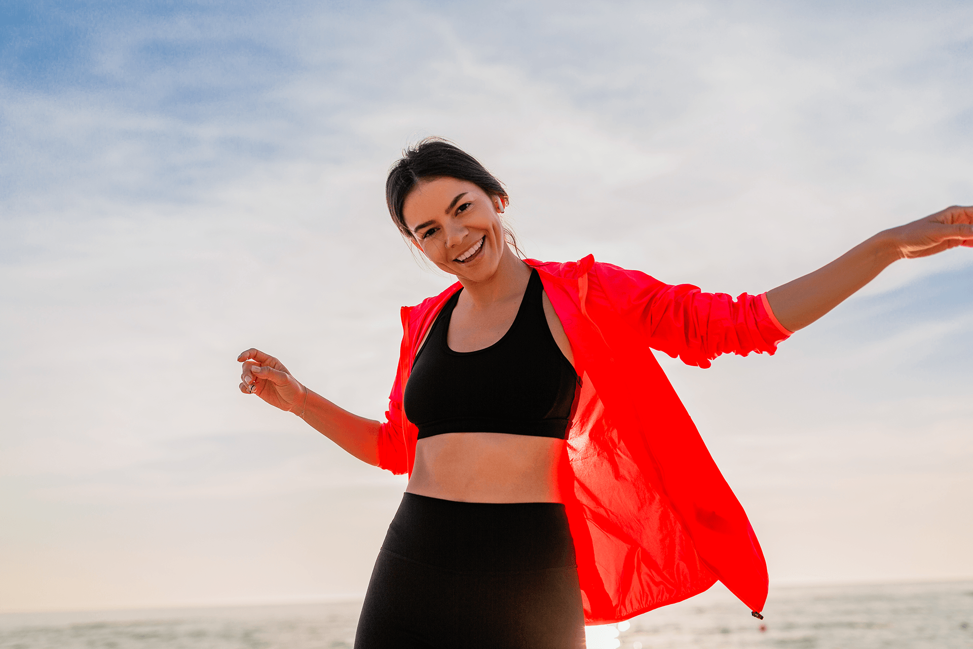 Energetic woman in athletic wear celebrating outdoors with arms outstretched
