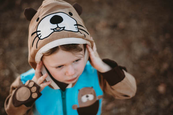 Child wearing brown otter costume hat and blue vest outdoors