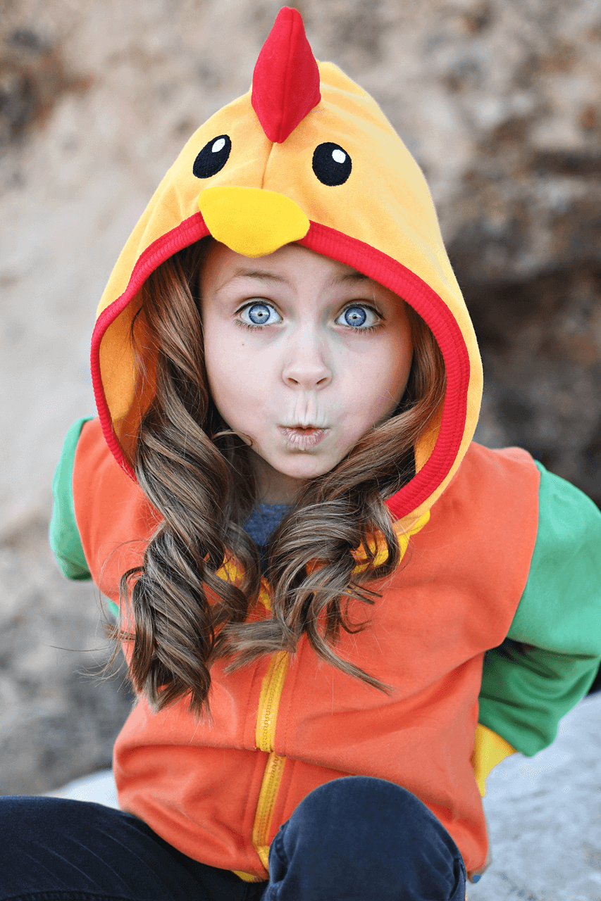 Child wearing colorful chicken costume hoodie with red crest and orange vest