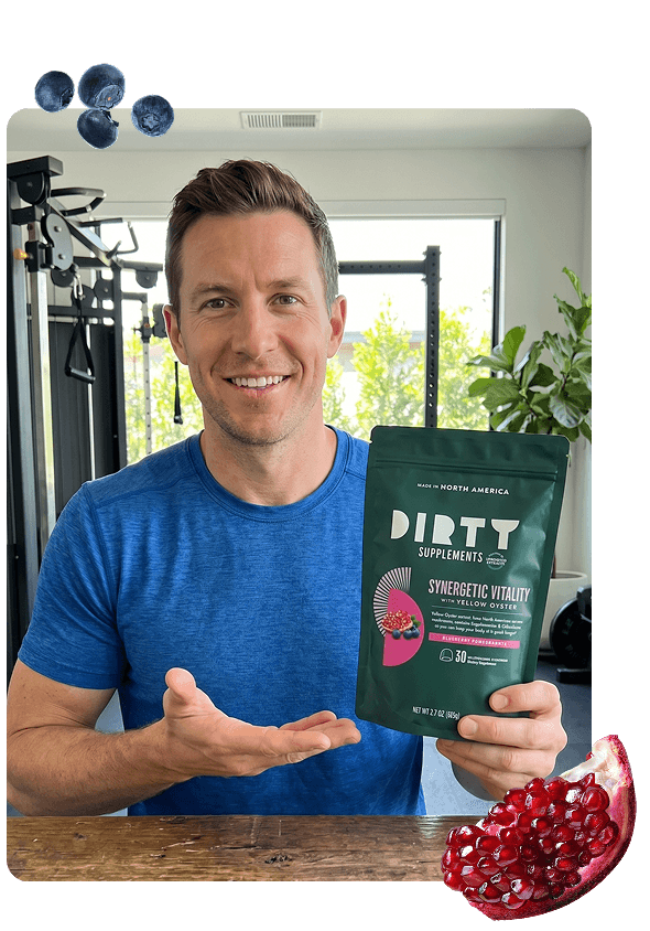 Man in blue shirt holding DIRTT Supplements Synergetic Vitality with Yellow Oyster Blueberry Pomegranate supplement pouch in a home gym setting