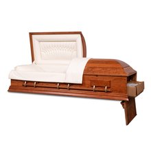 An open, empty casket presented at a three-quarter angle, set against a dark background. The casket's exterior is a warm, honey-toned wood with a polished finish and a series of ornamental bar handles along its side. The interior is lined with a cream-colored fabric, with the head end of the casket featuring a tufted design, giving it a look of comfort and tranquility.