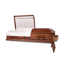 An angled view of an open, empty casket with a closed foot end, set against a dark background. The casket has a polished, reddish-brown mahogany finish and features sturdy metallic handles on the sides. Inside, it is lined with a soft, white cushioned fabric, and the headrest is elegantly tufted, providing a peaceful and dignified appearance.
